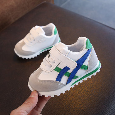 White children's sneakers with blue and green accents on a dark surface